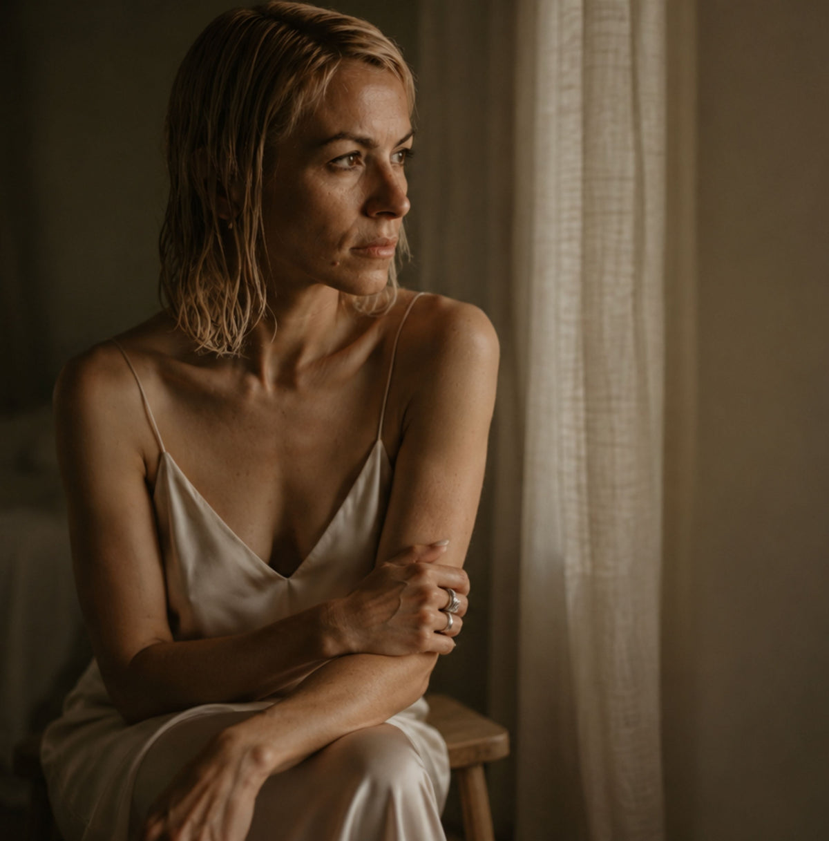 A woman wearing a light beige satin camisole and looking off-camera 