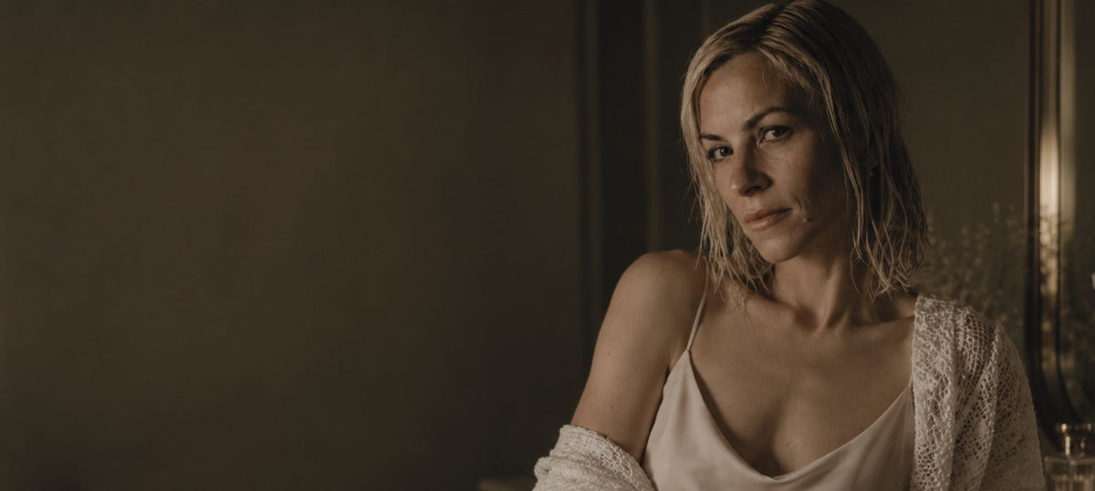 A woman with wet blonde hair wearing a cream camisole and a white knit cardigan