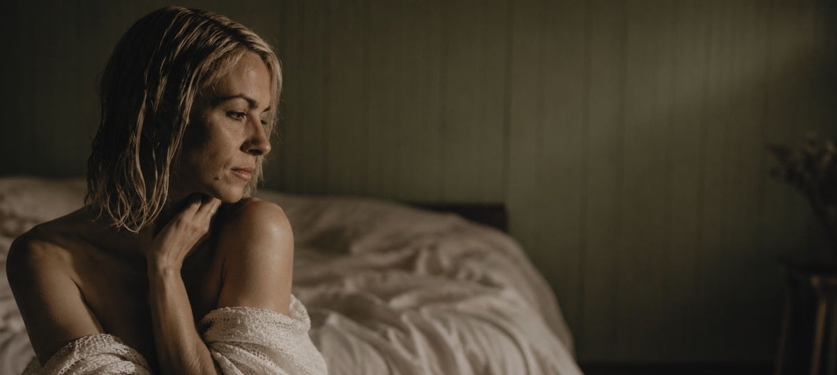 A woman with wet blonde hair sits on a bed