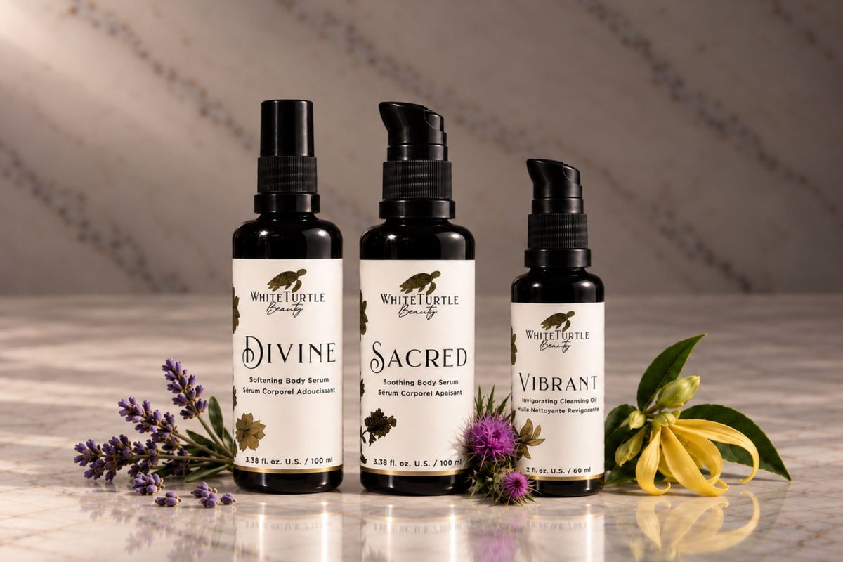 Three White Turtle Beauty body serum bottles labeled Divine, Sacred, and Vibrant, arranged on a marble surface 