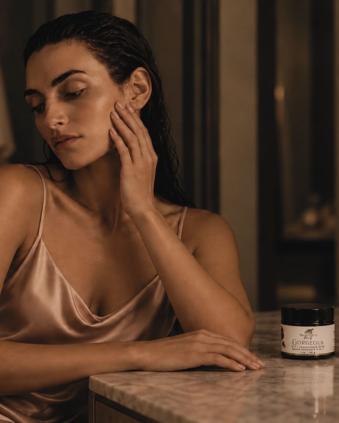 A woman touching her face, with a small jar of GORGEOUS balm next to her.