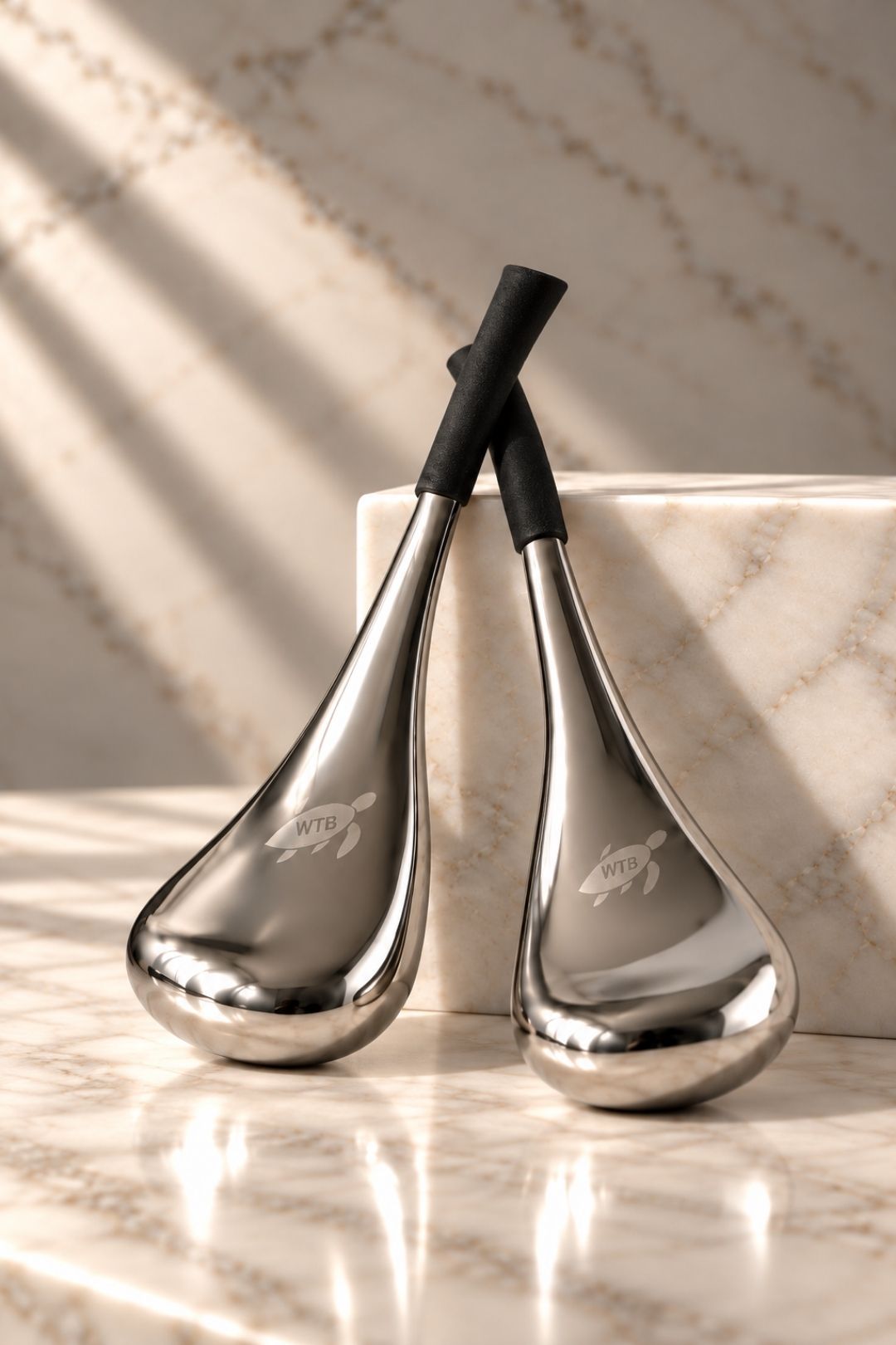 Two metallic massage tools with black handles and engraved turtle logos