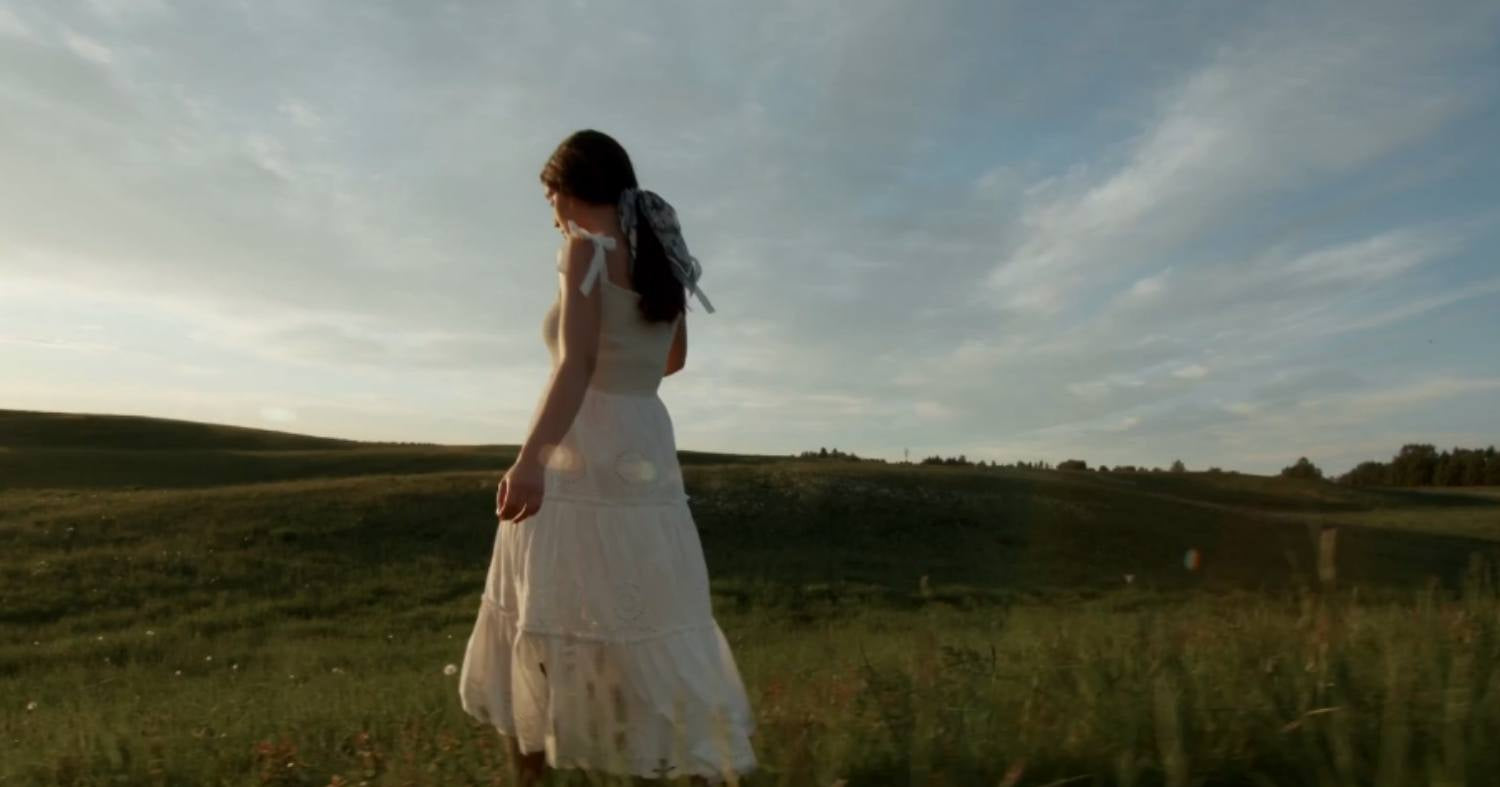 Woman in a white dress standing in a field with a sunset sky
