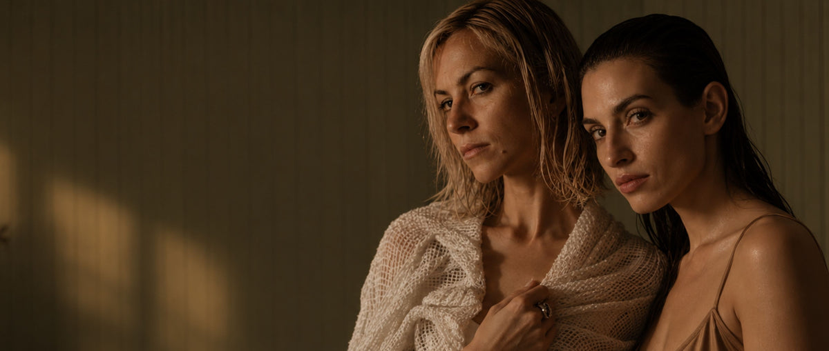 Two women looking stressed, with warm sunlight casting shadows on the wall behind them.