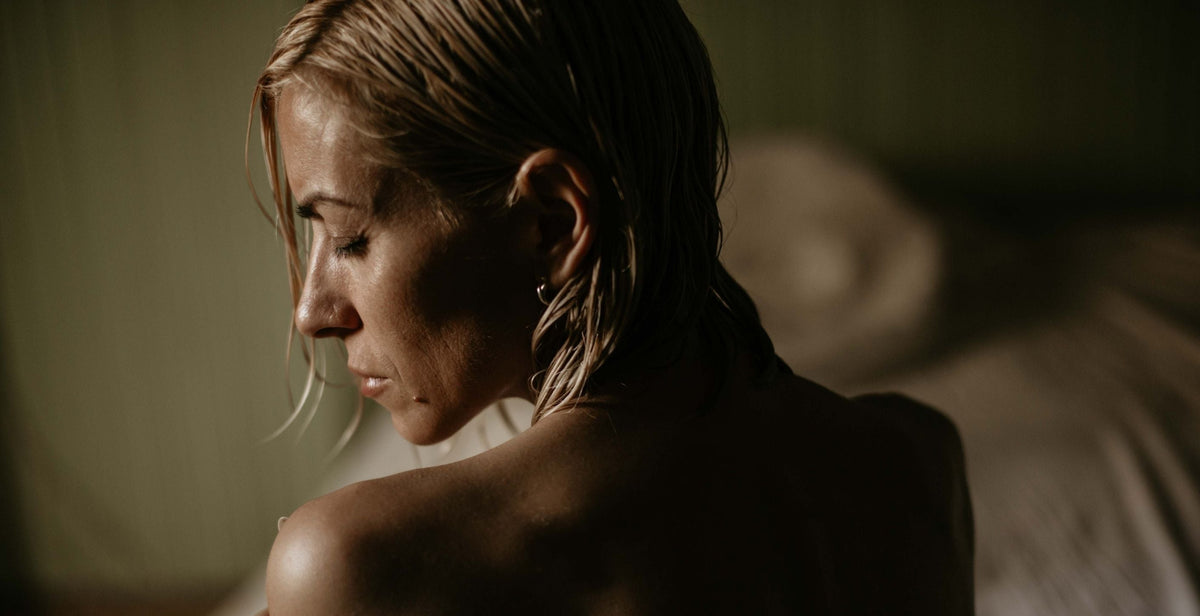A woman holding her shoulder in a moody, low-key photograph.